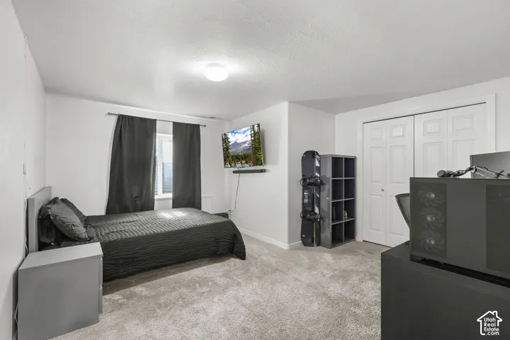 Window with blinds, wall-mounted light fixture, white interior walls, carpeted flooring, and bi-fold closet doors
