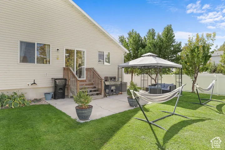 Expansive backyard featuring a manicured lawn, concrete patio, and a covered gazebo structure