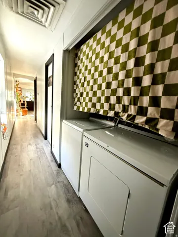 Laundry area with a full-size washer and dryer, adjacent to a hallway with wood-finish flooring