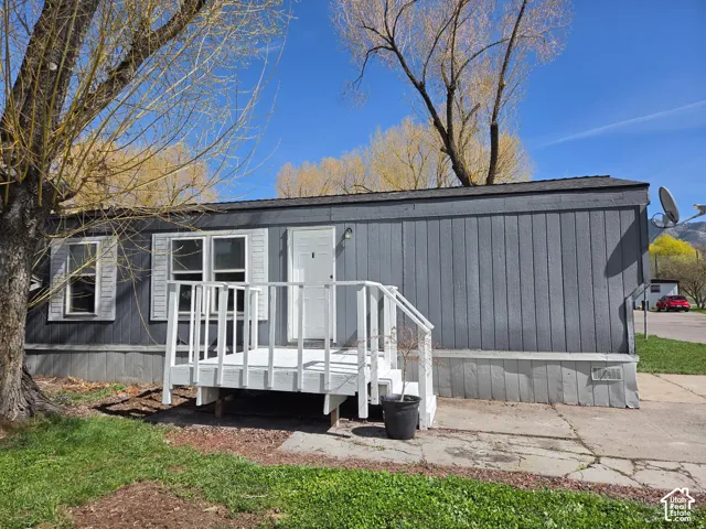 Exterior featuring gray vertical siding, white window shutters, and a white entry porch with railing