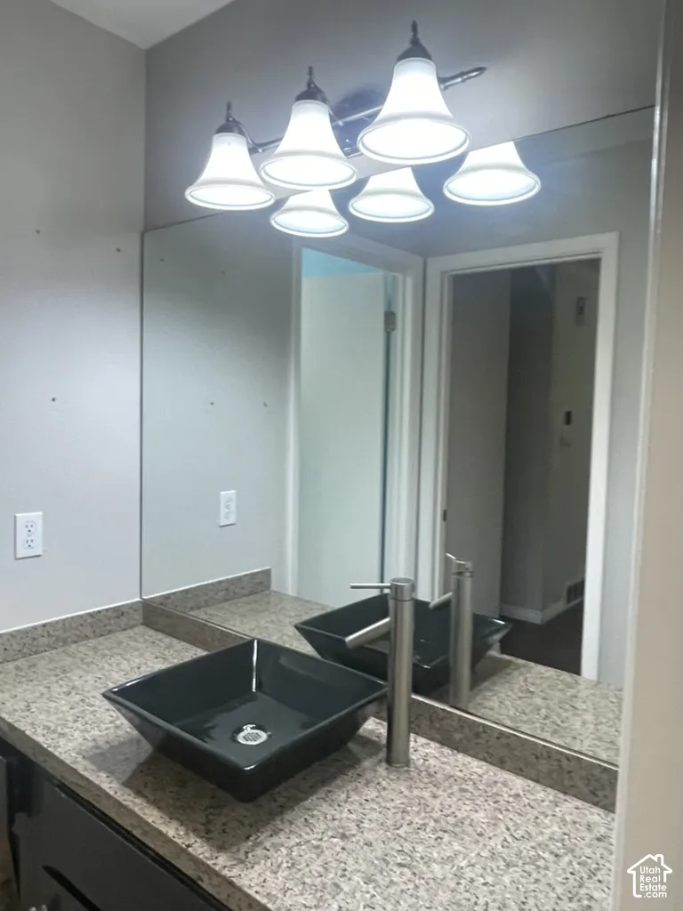 Square vessel sink with a tall single-handle faucet, set on a speckled countertop and dark cabinetry, illuminated by a multi-bulb vanity light fixture