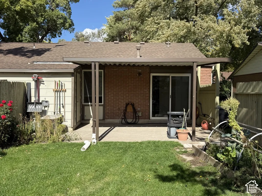Expansive backyard featuring a covered patio, brick exterior, sliding glass door, and a raised garden bed