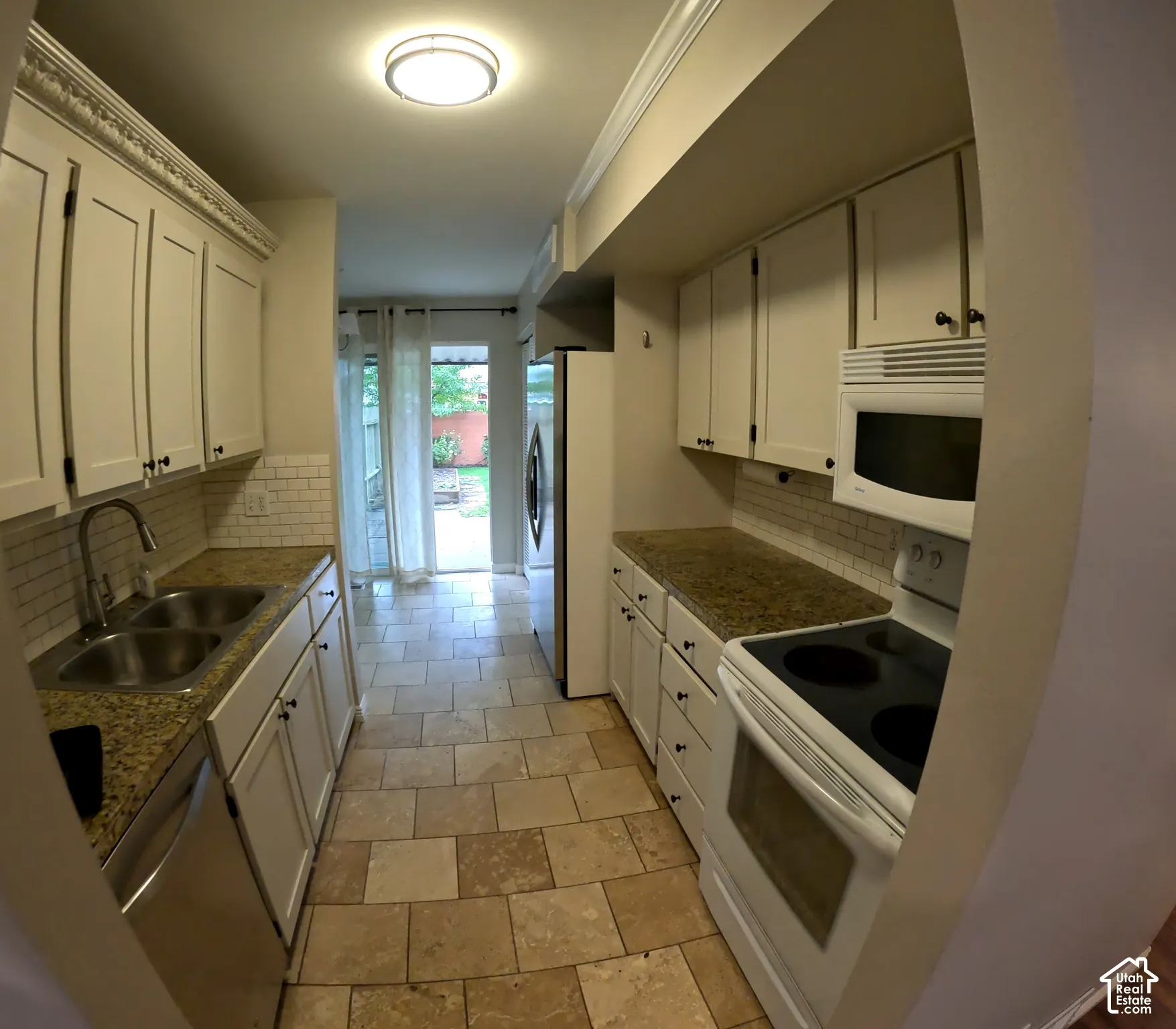 Galley kitchen featuring white cabinetry, light-toned countertops, subway tile backsplash, and tile flooring