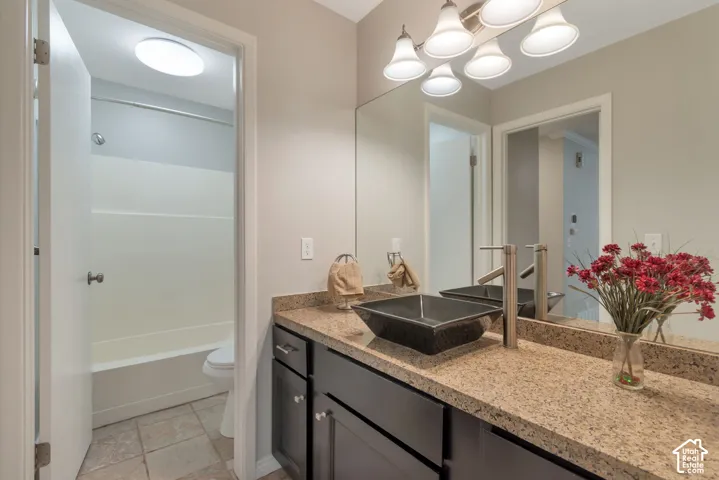 Vanity with square vessel sink set on a speckled countertop and dark cabinetry.