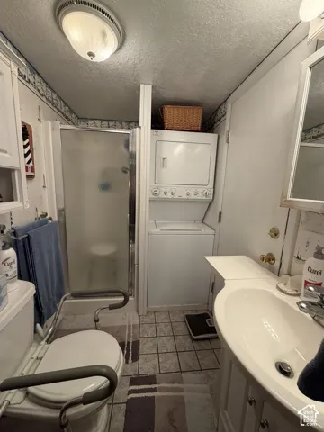 Compact bathroom featuring a shower enclosure, integrated stacked laundry appliances, vanity with a curved countertop, and a ceiling-mounted light fixture