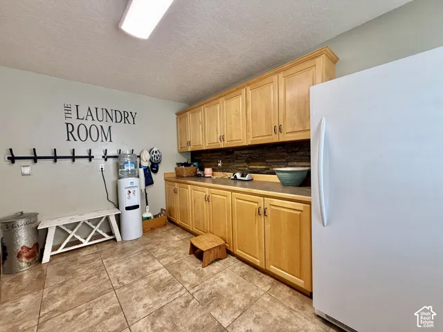 Spacious utility room featuring extensive natural wood-finish cabinetry, a durable countertop, and stone-look tile flooring