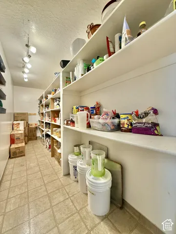 Expansive pantry featuring extensive built-in shelving, track lighting, and tiled flooring
