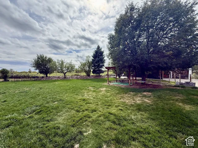 Expansive grassy yard featuring mature trees, a wooden pergola, and a decorative rock border