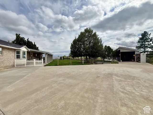 Expansive concrete driveway and parking area, brick exterior, covered porch, detached carport, and manicured lawn