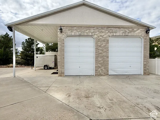 Two-car garage with white garage doors, light-colored brick exterior, and an attached carport