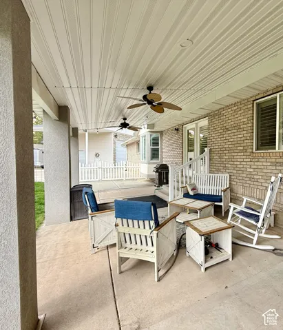 Covered concrete patio with two ceiling fans, brick exterior, and white picket fencing
