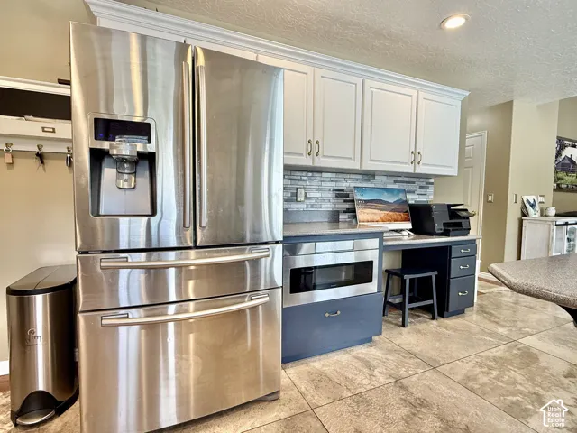 Stainless steel French door refrigerator, white upper cabinetry, mosaic tile backsplash, built-in microwave, and tile flooring