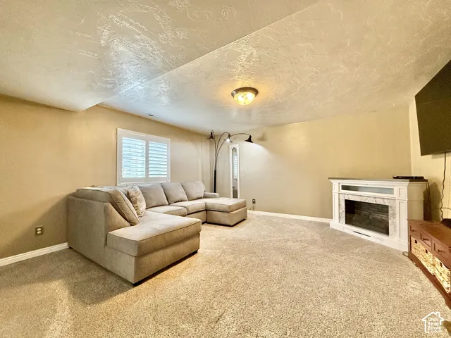 Carpeted flooring, corner fireplace with white surround, recessed window with plantation shutters, and flush mount lighting fixture