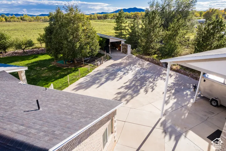 Expansive concrete driveway, attached carport, detached covered structure, green lawn, and mature trees