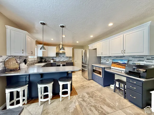 Spacious kitchen featuring two-tone cabinetry, a large peninsula with seating, stainless steel appliances, and a tiled backsplash