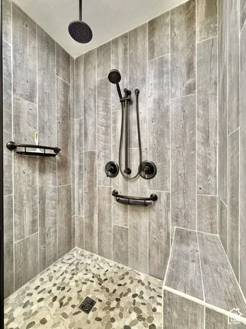 Shower with wood-look tile walls, pebble-stone flooring, a built-in bench, and a rain shower head