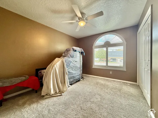Arched window with plantation shutters, ceiling fan with light fixture, textured ceiling, and bi-fold closet doors