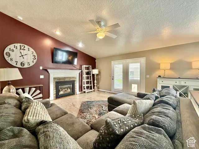 Vaulted ceiling with recessed lighting, stone-clad fireplace with mantel, tile flooring, and double french doors