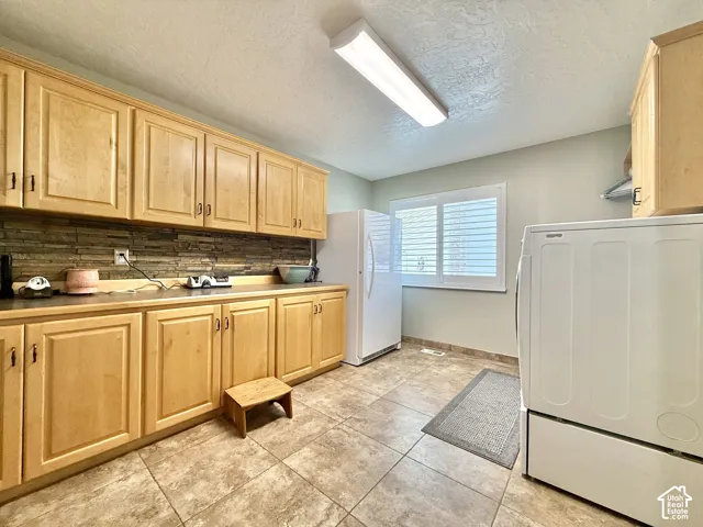 Light wood cabinetry with dark hardware, stone tile backsplash, and light-toned tile flooring