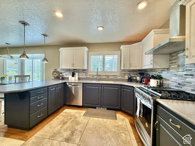 Kitchen featuring two-tone cabinetry, stainless steel appliances, mosaic tile backsplash, recessed lighting, and a peninsula with pendant lights
