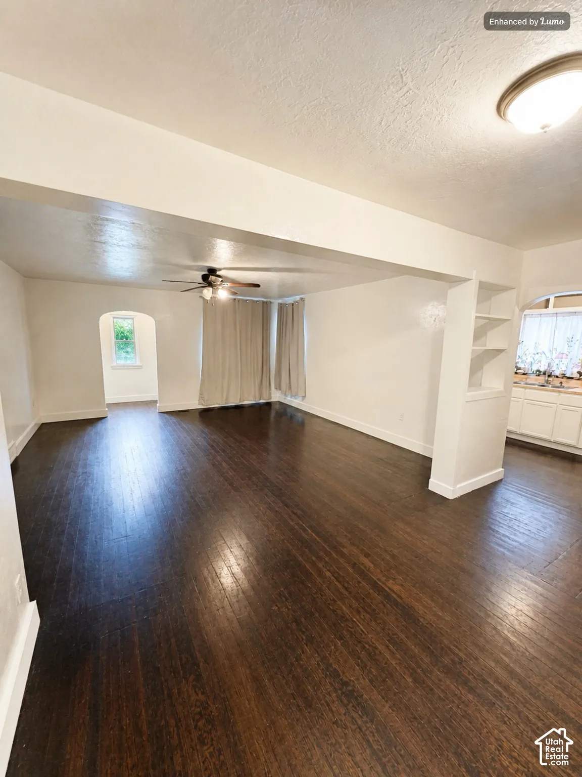 Dark wood-finish flooring throughout, ceiling fan with integrated lighting, recessed built-in shelving, and an arched doorway