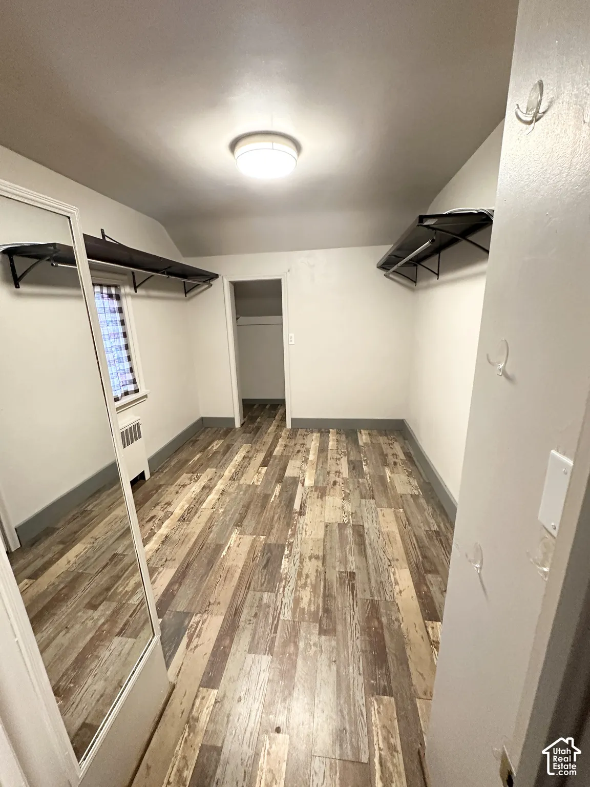 Wood-finish plank flooring, ceiling-mounted light fixture, built-in shelving, and a window with a radiator below