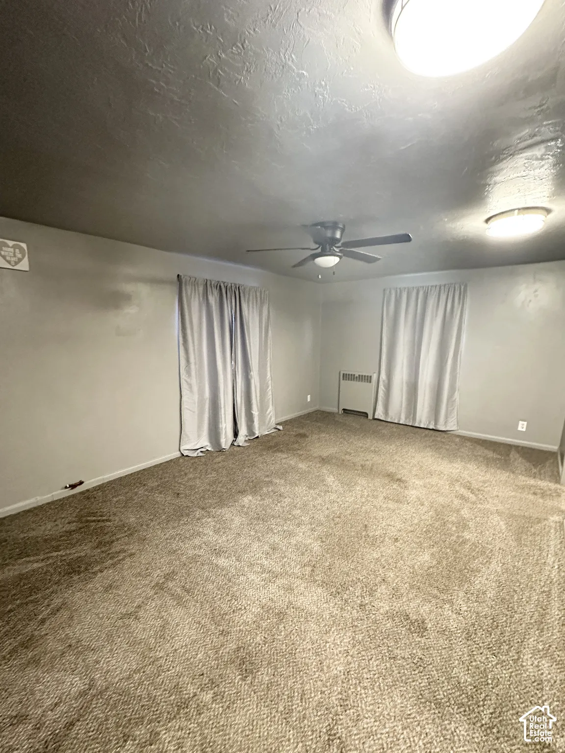 Carpeted flooring, ceiling fan, flush-mount ceiling light fixtures, and wall-mounted heating unit
