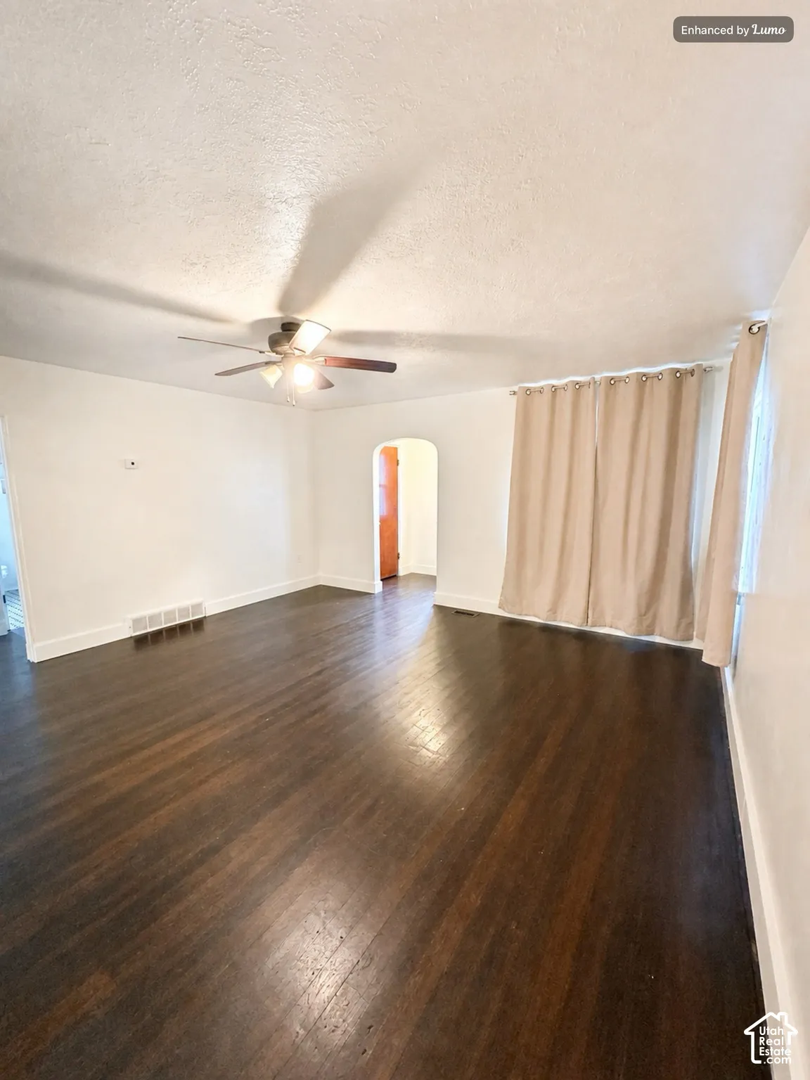 Dark wood-finish flooring with white baseboards, a ceiling fan, and an arched doorway
