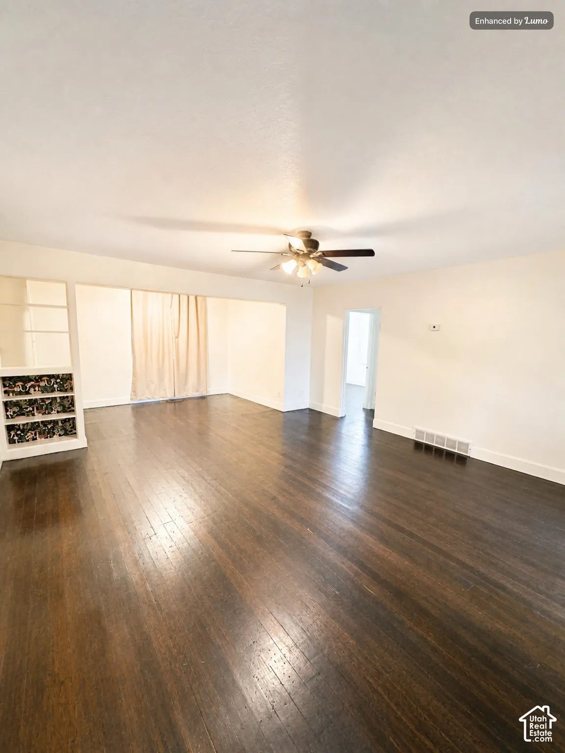 Dark wood-finish flooring throughout, ceiling fan with integrated lighting, and built-in shelving