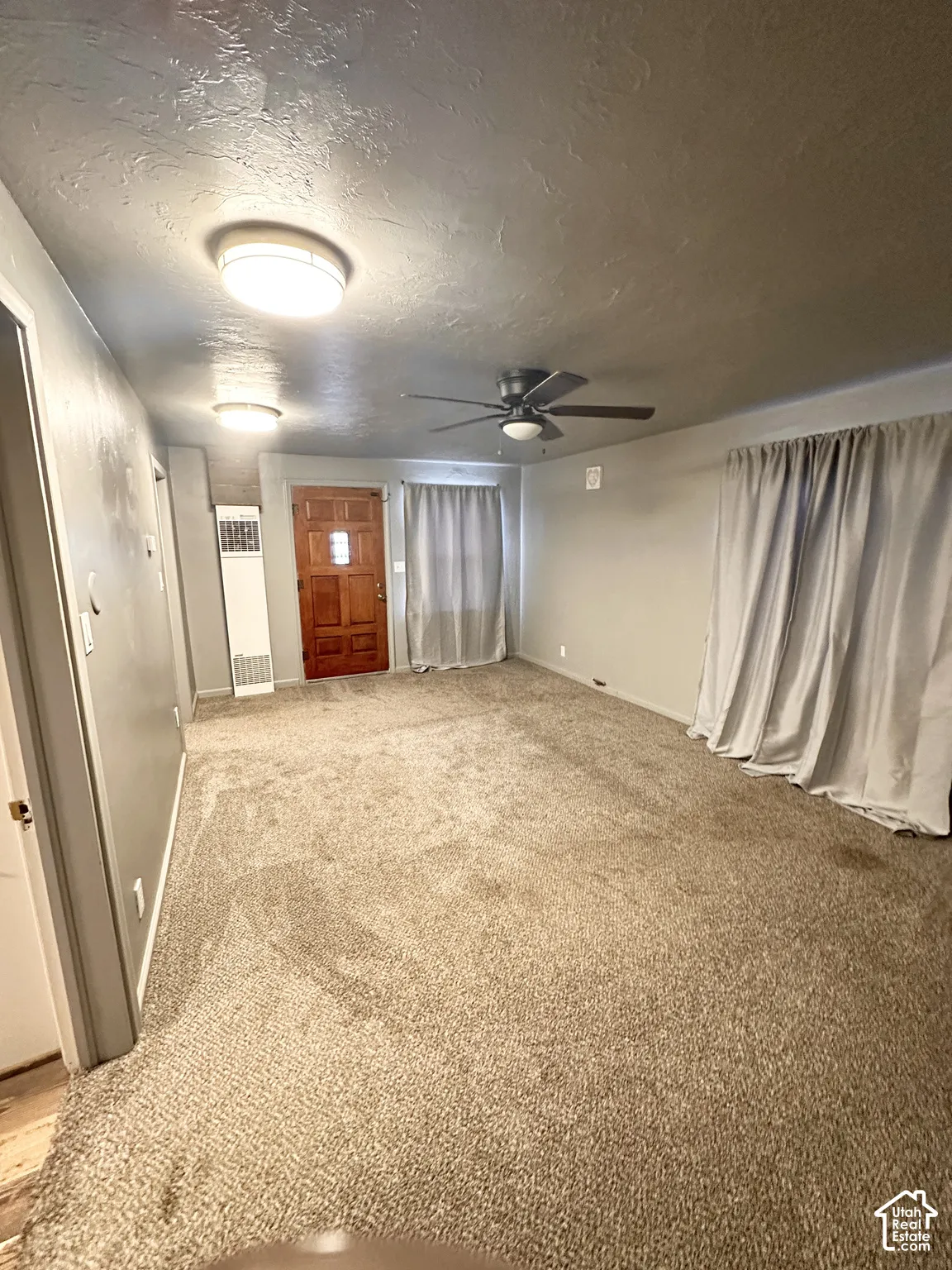 Spacious room featuring neutral carpeting, a dark wood-finish entry door, and a ceiling fan with integrated lighting