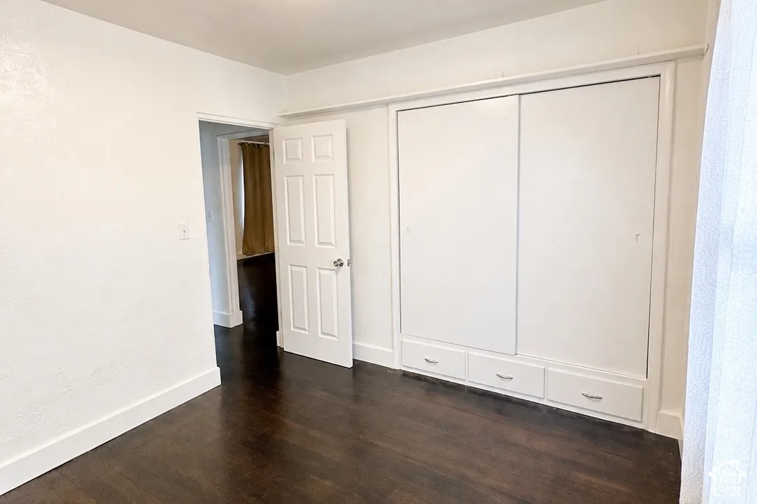 Dark wood-finish flooring with white baseboards, a flat white door, and built-in sliding closet doors with lower storage drawers