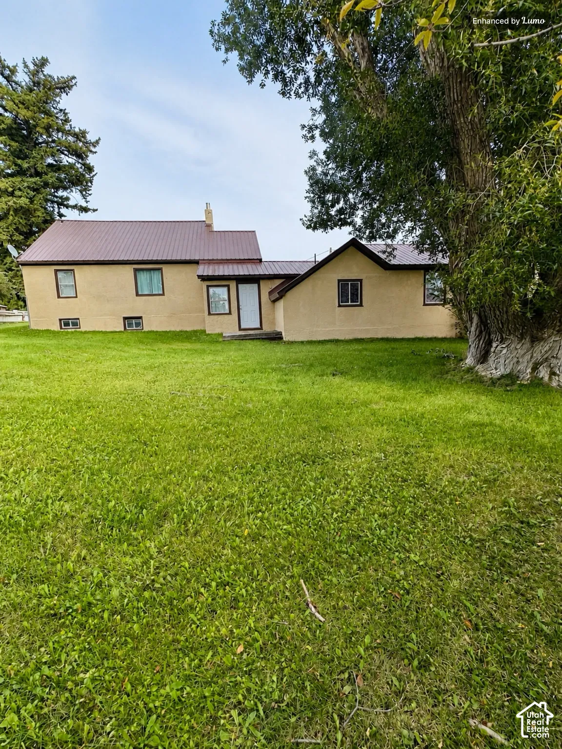 Expansive green lawn with mature trees and a stucco exterior residence featuring a brown metal roof