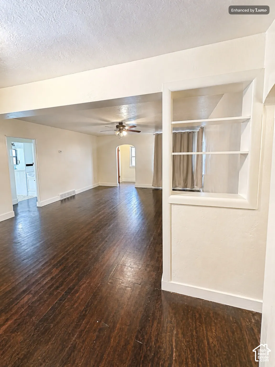 Rich wood-finish flooring throughout, integrated built-in shelving, and an archway opening to another room