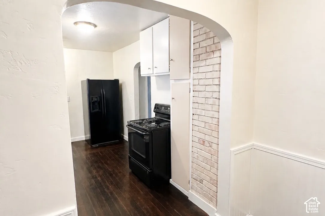 Kitchen featuring dark wood-finish flooring, white brick accent wall, white upper cabinetry, and a black range