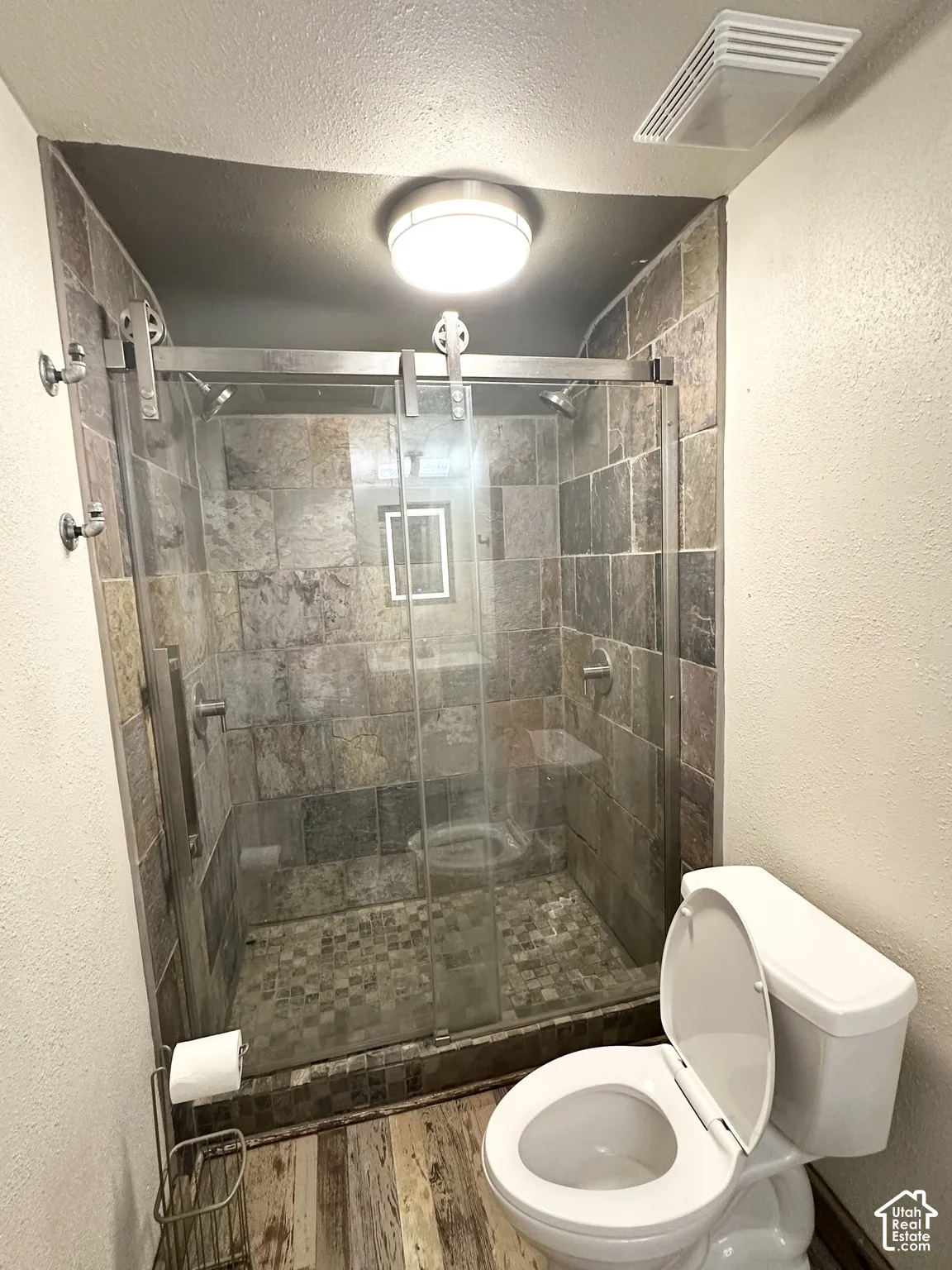 Glass-enclosed shower with stone tile surround and mosaic tile flooring