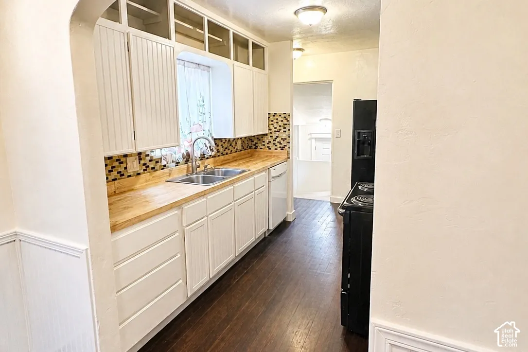 Kitchen featuring white cabinetry, wood-finish countertops, a mosaic tile backsplash, a double basin sink, and dark wood-finish flooring