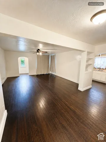 Dark wood-finish flooring throughout, ceiling fan with integrated lighting, recessed built-in shelving, and an arched doorway