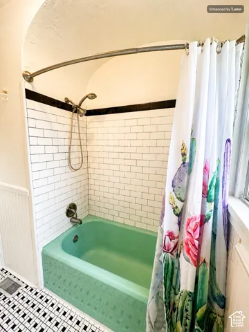 White subway tile shower surround with black accent trim, mint green bathtub, chrome shower fixture, and black and white mosaic tile flooring