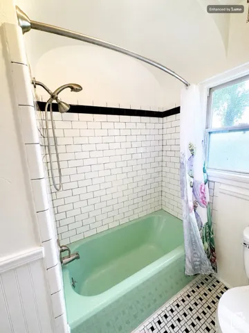 Subway tile shower surround with black accent band, green tub, and mosaic tile flooring