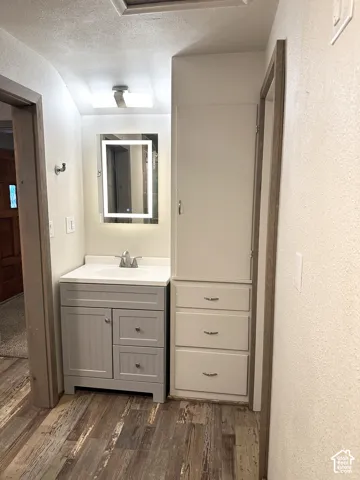 Wood-finish flooring with a modern vanity, integrated sink, and illuminated mirror