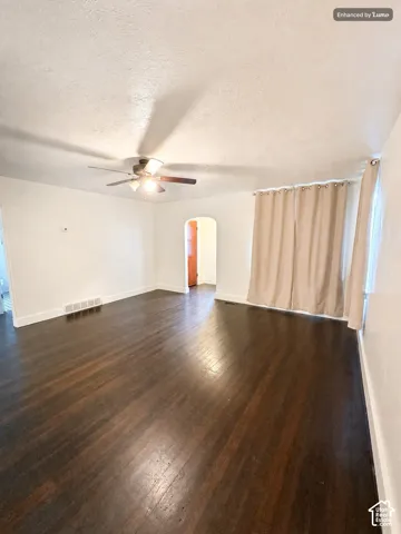 Dark wood-finish flooring with white baseboards, a ceiling fan, and an arched doorway