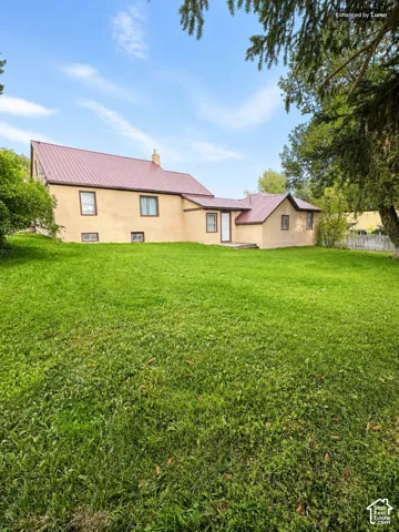 Expansive lawn surrounds a residence featuring a brown metal roof, light-colored stucco exterior, and multiple windows