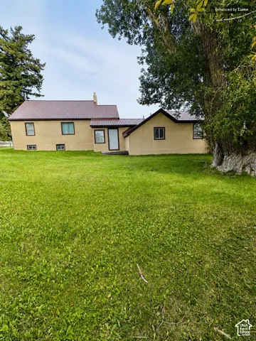 Expansive green lawn with mature trees and a stucco exterior residence featuring a brown metal roof