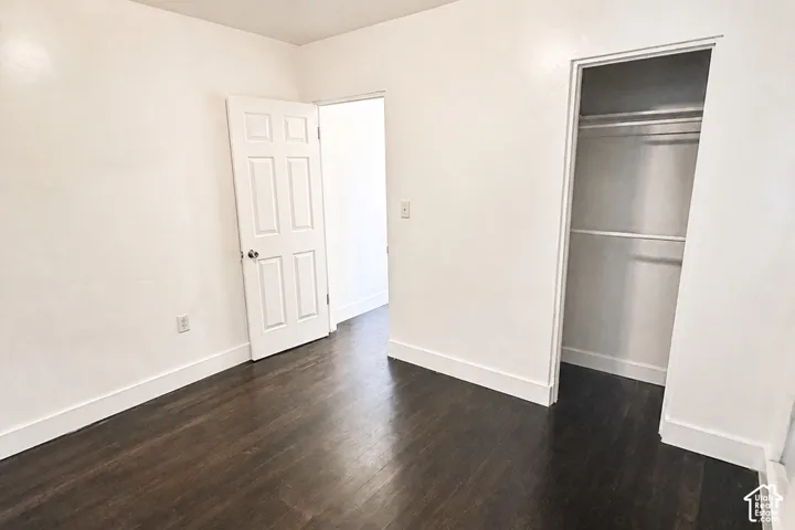Hardwood-style flooring with a dark finish, white walls, and a built-in closet with shelving