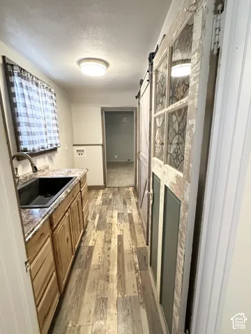 Wood-finish flooring, wood cabinetry, black sink, and a stained glass barn door