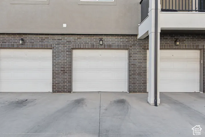 Three white garage doors with overhead lighting, gray brick facade, and concrete drive