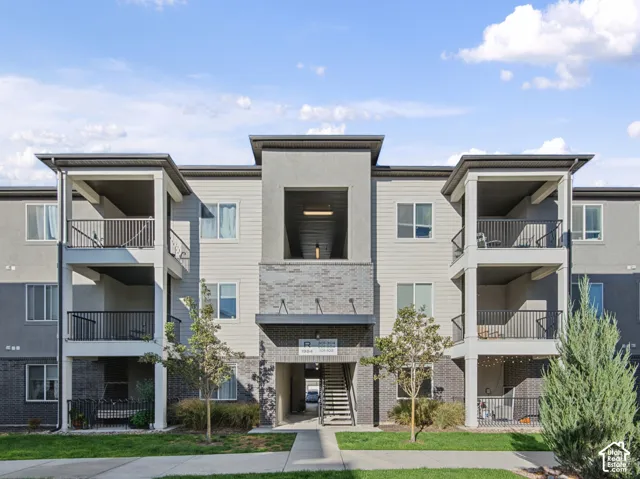 Multi-story building with a stucco and siding exterior, featuring multiple balconies with black railings, and a central entryway with stone accents
