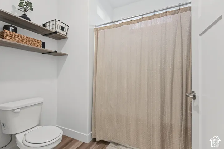 White wall finishes, wood-finish flooring, two floating shelves with black brackets, and a white toilet