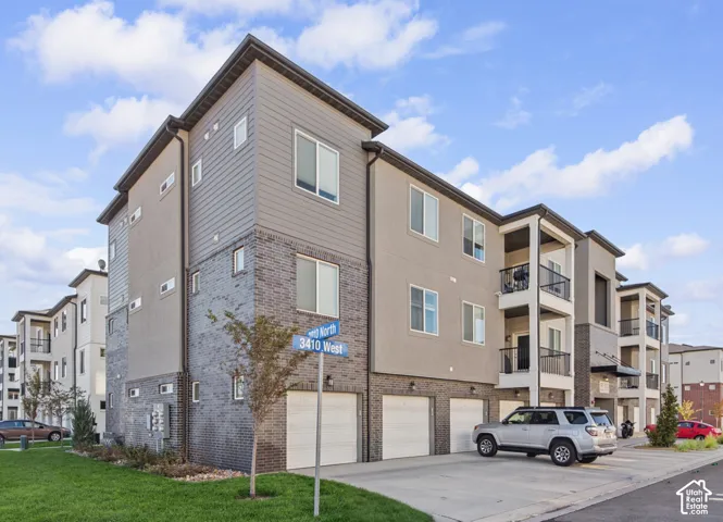 Modern multi-story building featuring integrated garages, private balconies with dark railings, and a façade combining brick and siding finishes