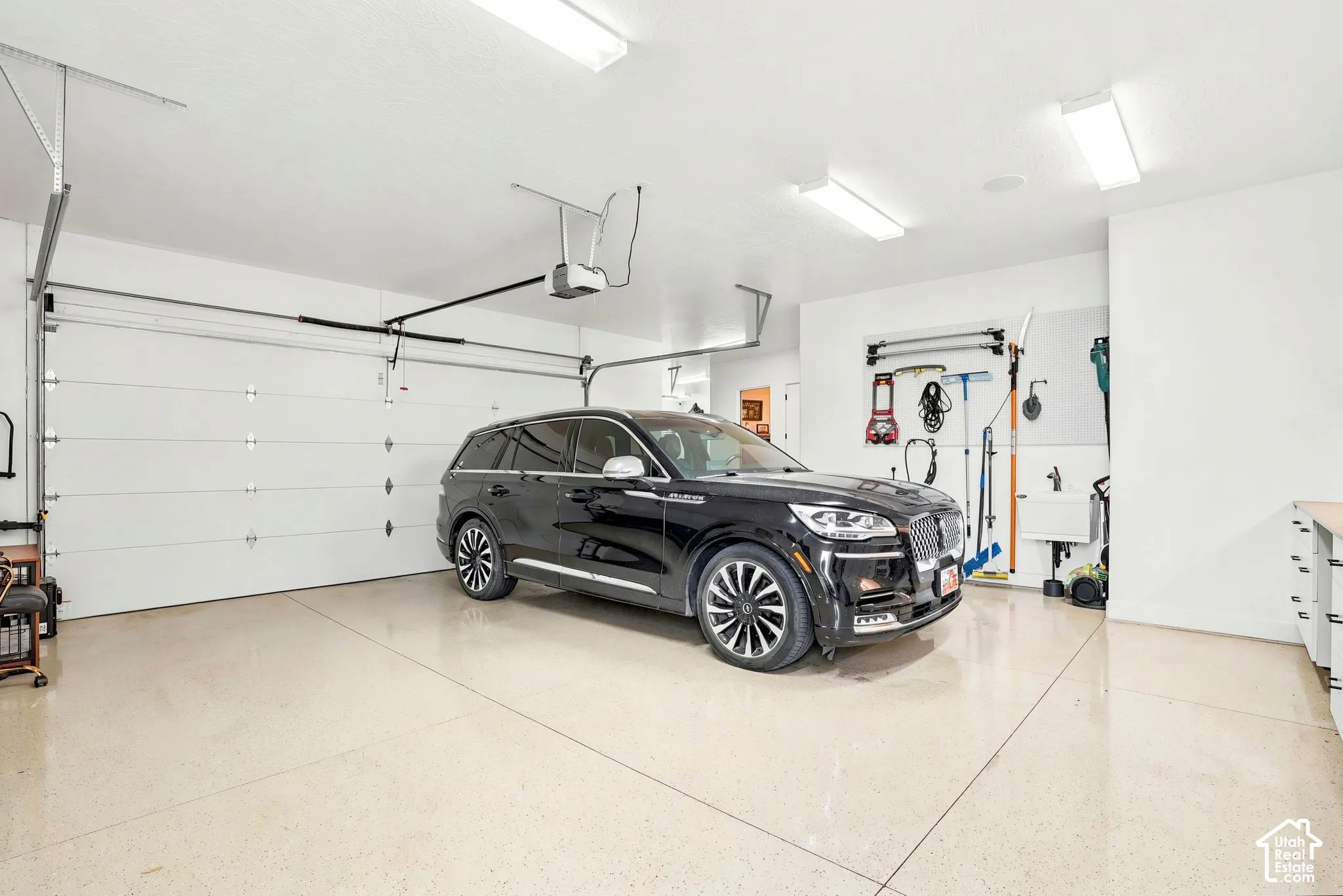 Two-car garage featuring a light-toned epoxy floor finish, overhead lighting, and white walls